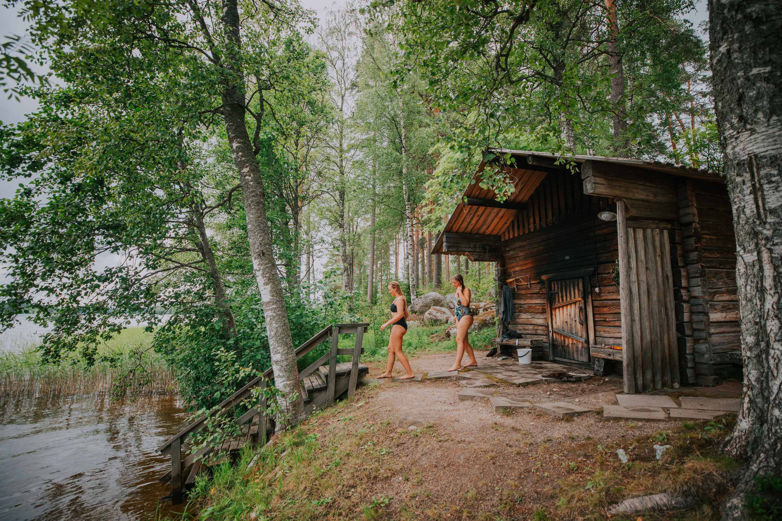 Two persons walking towards a lake from a sauna.