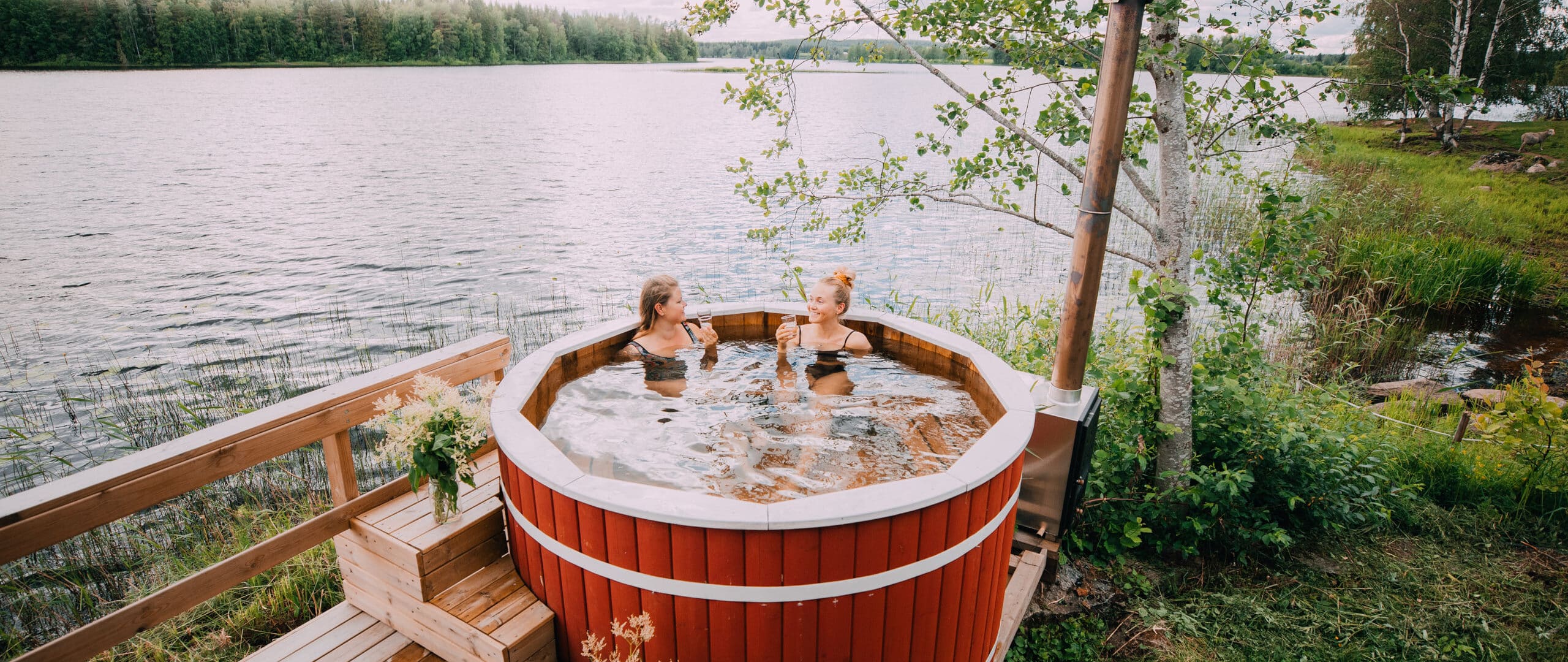 Two persons in an outdoor hot tub located next to a lake.