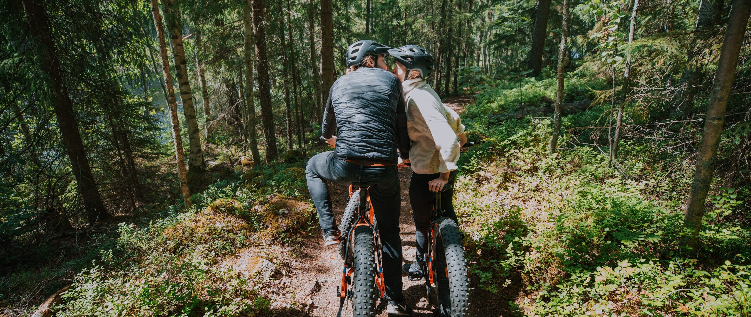Two persons in a forest, kissing while on fatbikes.