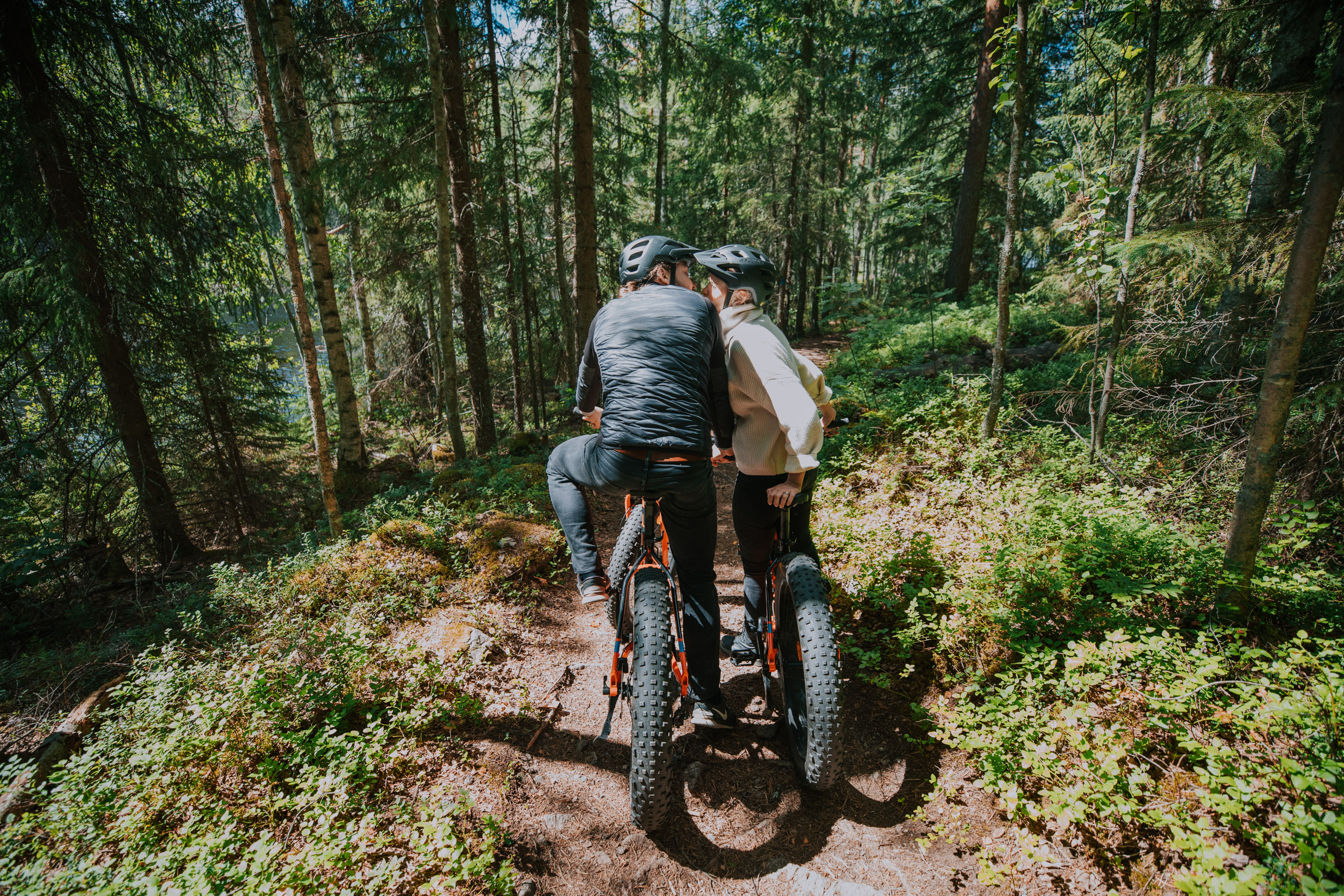 Two persons in a forest, kissing while on fatbikes.