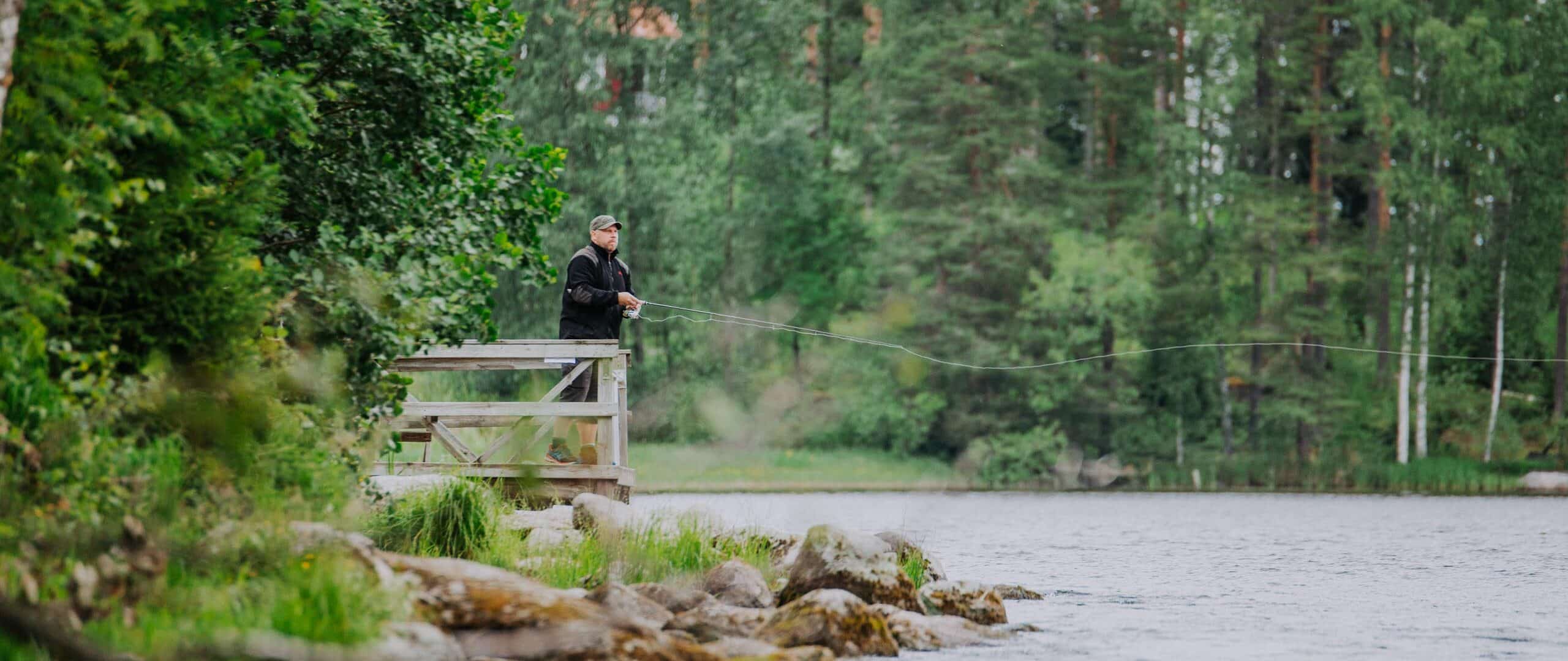 Person fishing from a river while standing on a wooden platform.