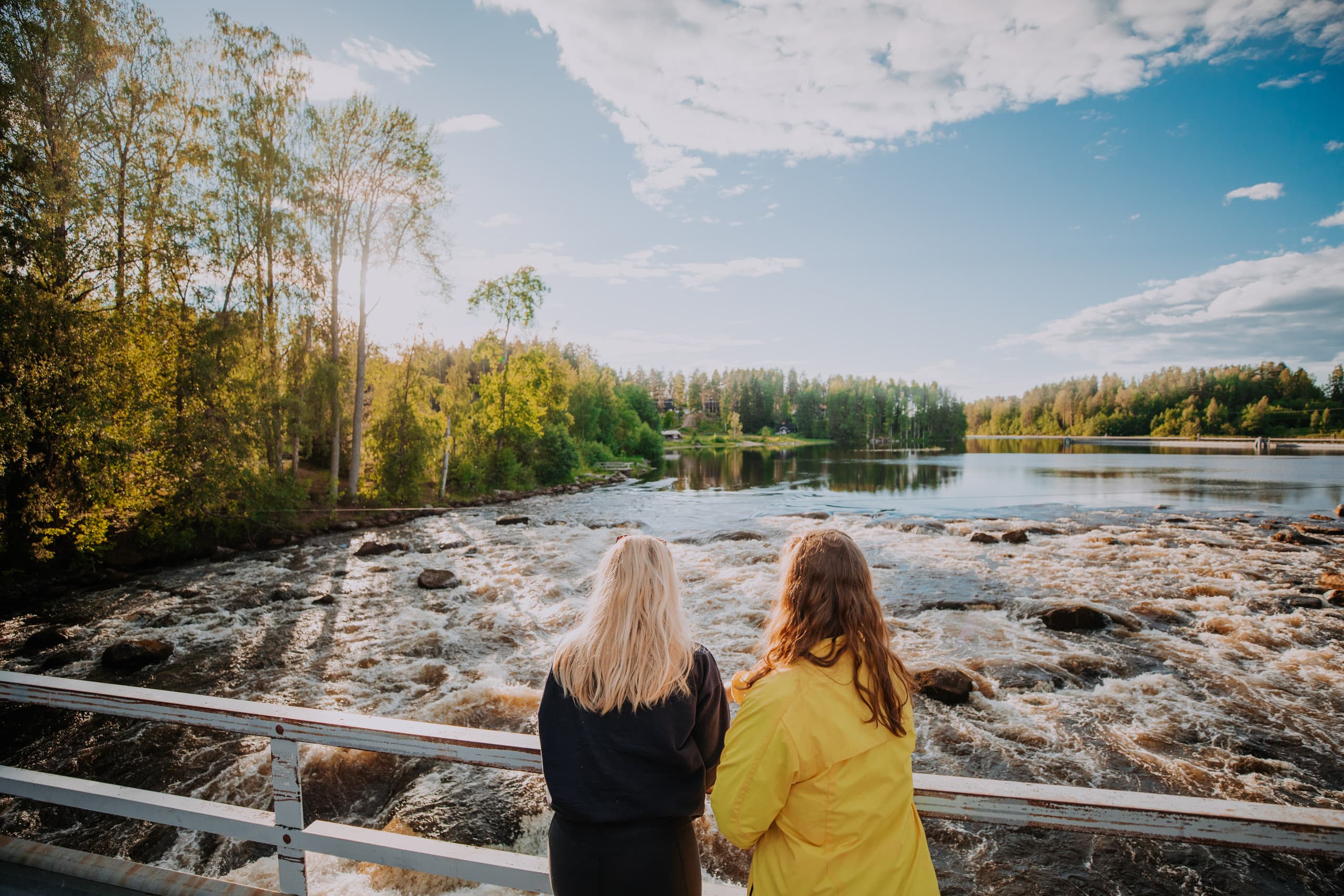 Two persons on a bridge that goes over rapids.