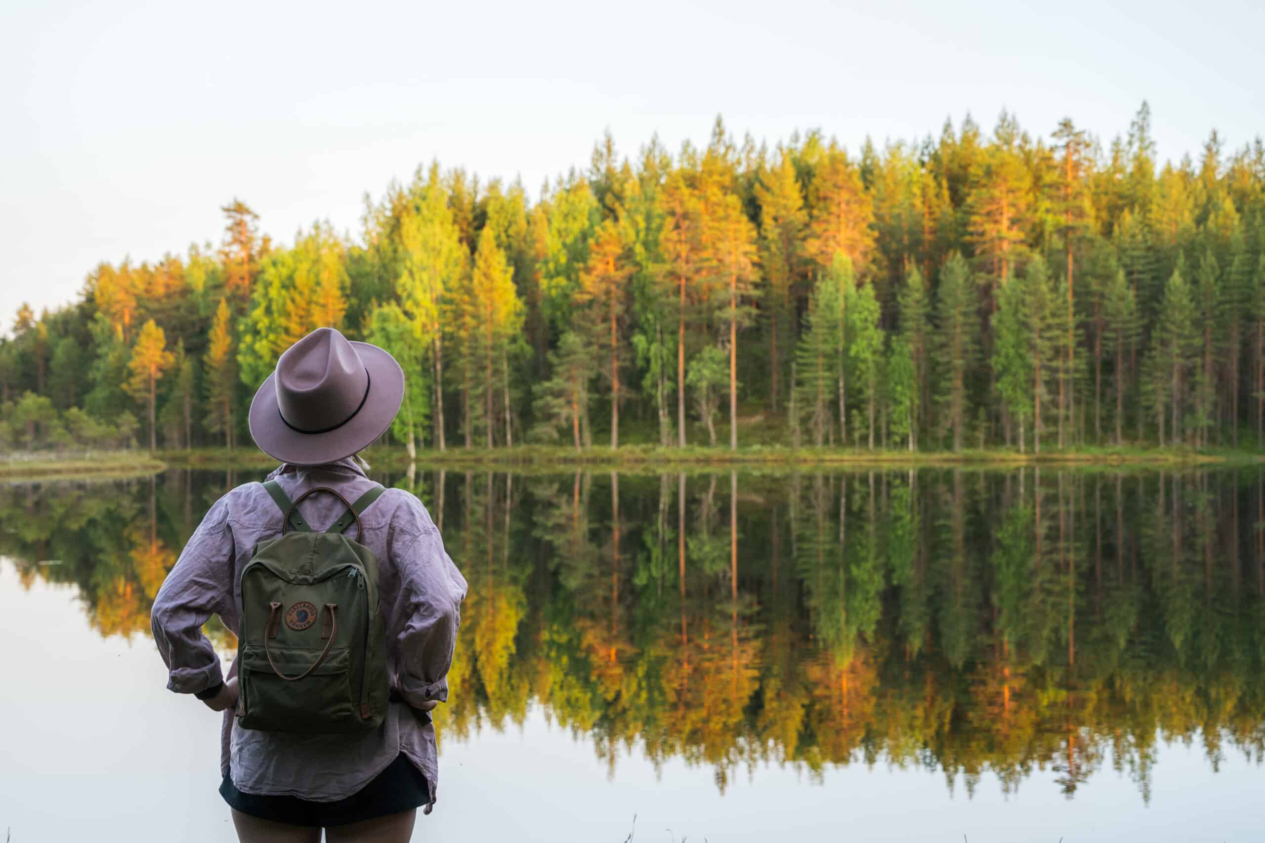 Person standing in front of a lake and forest.