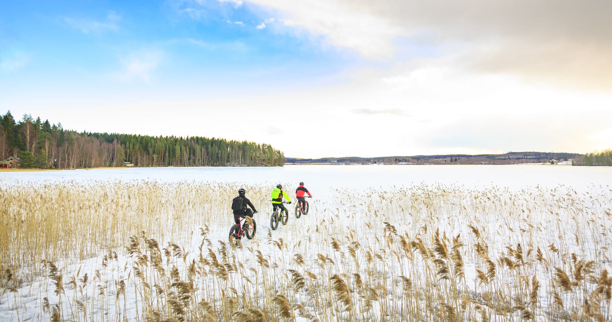 Three persons cycling on a snowy and frozen lake.