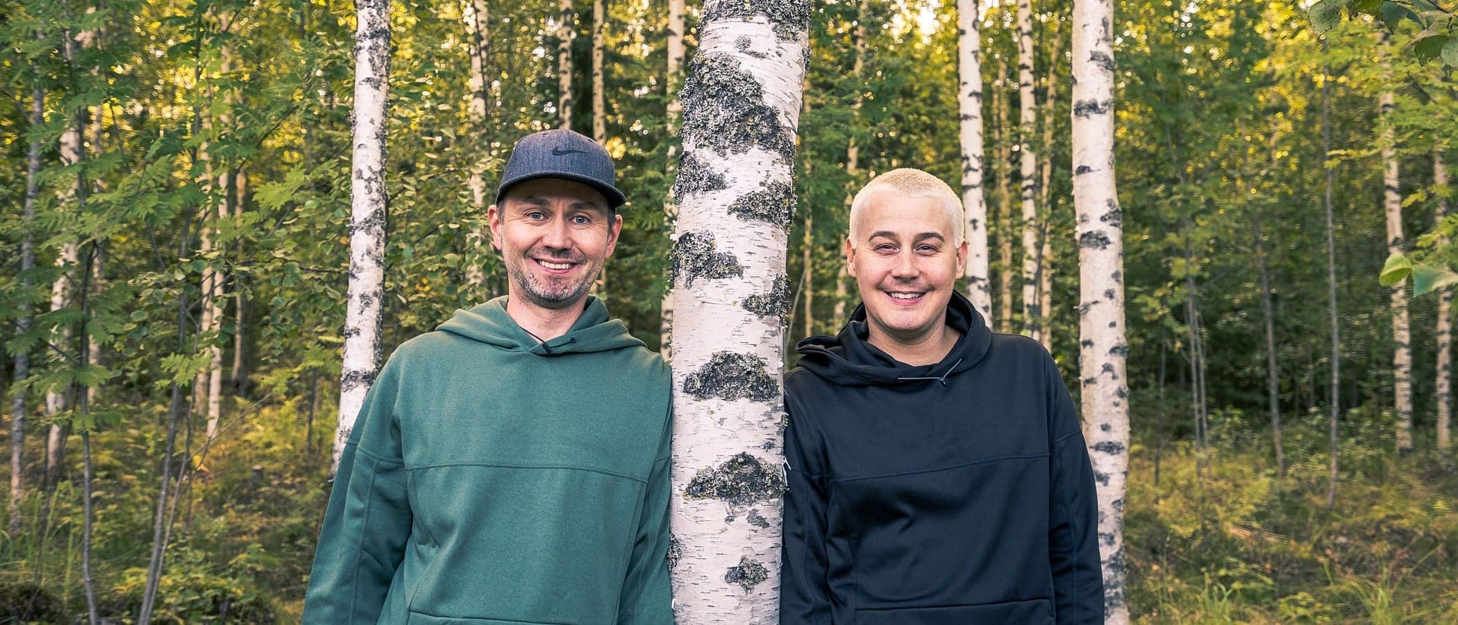 Two persons leaning against a tree and smiling.